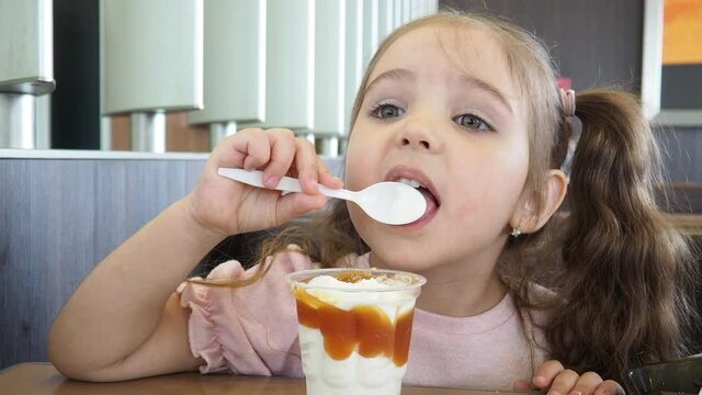 Happy surprised little girl serving ice cream .The child sits at a table in a cafe and is happy A happy childhood. cute beautiful girl eating ice cream in a cafe. sweets. family vacation. positive emo