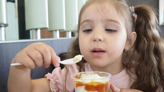 Happy surprised little girl serving ice cream .The child sits at a table in a cafe and is happy A happy childhood. cute beautiful girl eating ice cream in a cafe. sweets. family vacation. positive emo