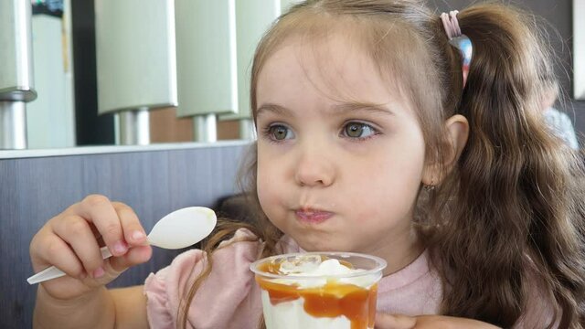 Happy surprised little girl serving ice cream .The child sits at a table in a cafe and is happy A happy childhood. cute beautiful girl eating ice cream in a cafe. sweets. family vacation. positive emo