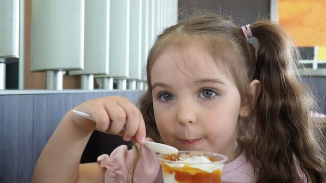 Happy surprised little girl serving ice cream .The child sits at a table in a cafe and is happy A happy childhood. cute beautiful girl eating ice cream in a cafe. sweets. family vacation. positive emo