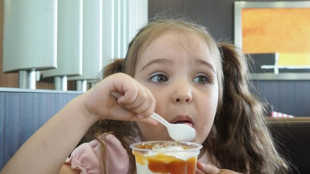 Happy surprised little girl serving ice cream .The child sits at a table in a cafe and is happy A happy childhood. cute beautiful girl eating ice cream in a cafe. sweets. family vacation. positive emo
