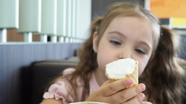 Happy surprised little girl serving ice cream .The child sits at a table in a cafe and is happy A happy childhood. cute beautiful girl eating ice cream in a cafe. sweets. family vacation. positive emo