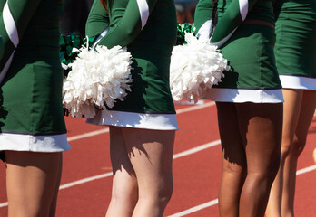 Close up of cheerleaders holding pom poms behind backs
