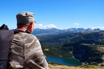 Fototapeta na wymiar an adult man sits with a backpack on the top of a mountain and looks from above at a mountain lake