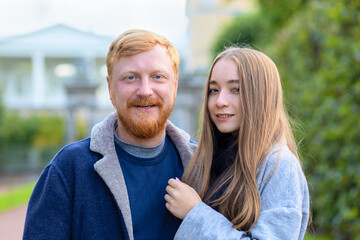 Happy mixed race couple of millennial, diversity, redhead ginger bearded caucasian man and asian girl in park looking at the  camera.