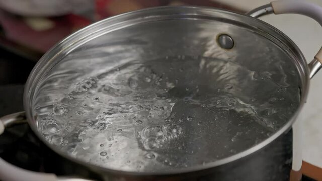 clean transparent hot water boiling in stainless steel pot - slo-mo close-up