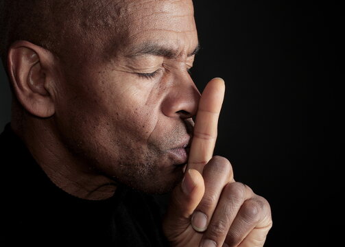 man with finger over mouth gesture keeping quiet on black background stock photo