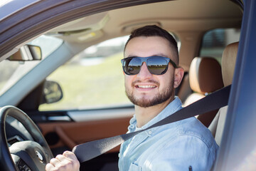 Smiling handsome young man adjusting seat belt in car.