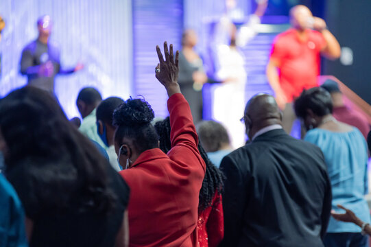 African American Woman in a Red Outfit with Her Hand Raised in Church During Praise and Worship