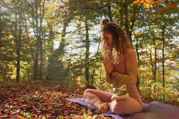 latin woman with tattoos performing yoga and meditation in the lotus pose in a forest during...
