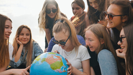 A group of cheerful girls is exploring the globe of the world in the meadow.