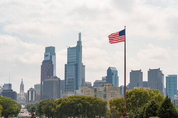 Skyline of Philadelphia financial downtown and City Hall Clock Tower at summer day time, Pennsylvania, USA. Hovering United States flag on the hot wind blow.