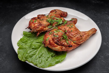 Fried tobacco chicken with a leaf of lettuce on a plate, on a dark background