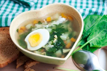 Fototapeten Green borsch with sorrel, parsley, egg and grens in the bowl form of heart with spoon on wooden background © Yana Staryk