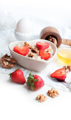 Breakfast with oatmeal with strawberries, honey, walnuts and egg on white background. Breakfast for child. Oatmeal in a white heart-shaped bowl
