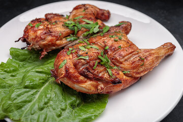Fried tobacco chicken with a leaf of lettuce on a plate, on a dark background