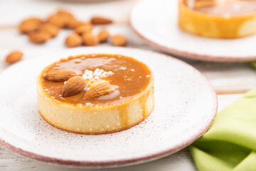 Sweet tartlets with almonds and caramel cream with cup of coffee on a white wooden background. side view, selective focus.