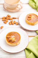 Sweet tartlets with almonds and caramel cream with cup of coffee on a white wooden background. side view, selective focus.