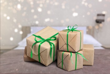 Boxes with Christmas gifts on the bed with a white blanket and pillow. The bedroom is decorated with Christmas lights.