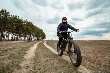 A man rides through the countryside on an electric bike with thick wheels. Sports hobby.