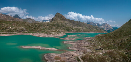 Mountain panorama at the reservoir lake Lago Bianco at the Bernina Pass with blue sky and sun from above in summer.