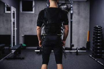 Fototapeta na wymiar The future and the revolution in training, electrical muscle stimulation. A close-up shot of a man's body in a black suit with cables for EMS technology standing in a gym with a dark gray atmosphere