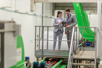 Running a business in a factory. A man and a woman in an elegant suit inspect the work of the washing machine and sorting the fruit. Tablet data reading and quality control, apple production