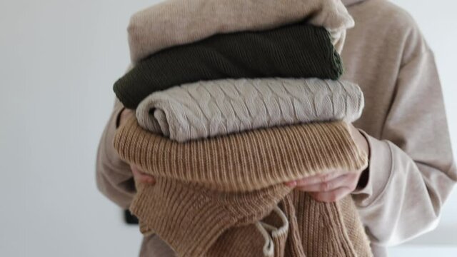 Woman's hand holding a stack of clothes. Clothes Donation, Renewable Concept.Preparing Garment at Home before Donate. Woman packs clothes for a donation or for moving