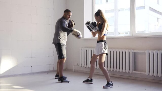 Father is preparing his young daughter for mixed martial arts competitions. The girl hits a punching bag
