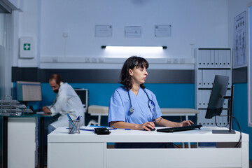 Medical assistant using keyboard and computer at office for healthcare system. Woman nurse looking at monitor screen for assistance and support, working late at night. Health specialist