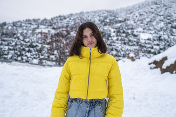 Fototapeta na wymiar young woman in yellow coat chilling outside in snowy weather,young woman smiling at camera in front of natural background in snowy weather
