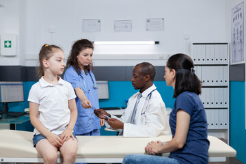 Obraz premium Therapist woman nurse giving lungs radiography to african american pediatrician doctor during child appointment in hospital office. Physician man explaining medical expertise. Health care service