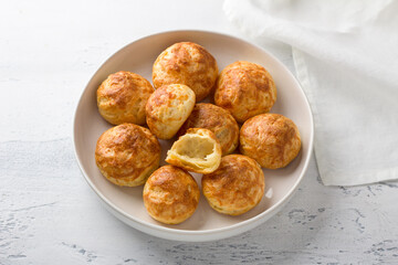 Cheese profiteroles, gougeres, traditional French pastries, in a white plate on a light gray background, top view