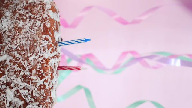 Vertical video of a caucasian hand burying some birthday candles in a cake and some birthday stuff with a pink background 