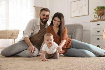 Happy parents watching their baby crawl on floor at home