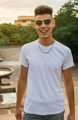 Obraz premium Young person with sunglasses smiling happily in a square that has a fountain underneath and overlooks an avenue