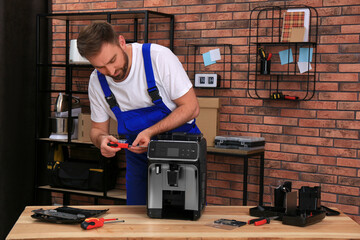Repairman with screwdriver fixing coffee machine at table indoors