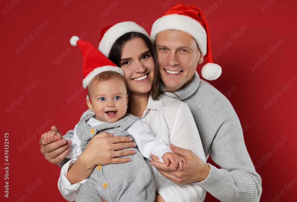 Canvas Prints Happy couple with cute baby wearing Santa hats on red background. Christmas season