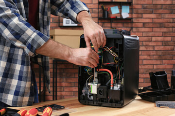 Man with screwdriver fixing coffee machine at table indoors, closeup