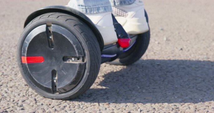 Woman in blue jeans and white snickers learns to ride black hoverboard with marked wheels ON asphalt track on sunny day close view