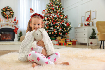 Obraz na płótnie Canvas Cute little girl with toy bunny in room decorated for Christmas