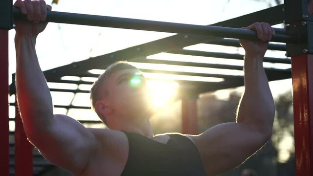 Muscular man doing pullups on sunset sky background. Calisthenics, healthy lifestyle and workout concept 