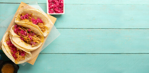 Pork meat tacos called cochinita pibil on a turquoise background. Mexican food