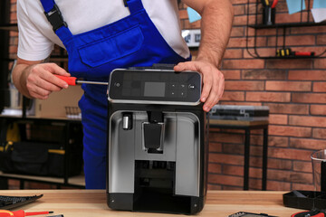 Repairman with screwdriver fixing coffee machine at table indoors, closeup