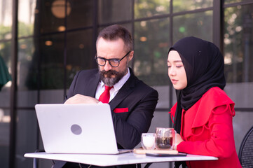 Businessman caucasian and business woman Muslim discussing, consulting, exchanging ideas, analyzing, considering, reasoning about work.