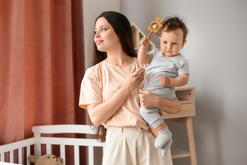 Young mother holding cute little baby with rattle at home
