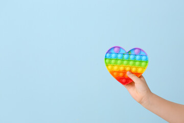 Child hand with heart shaped pop it fidget toy on color background
