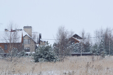 Fototapeta na wymiar Cottage village near a forest in the countryside. Cloudy winter day. Weekend rest. Winter house