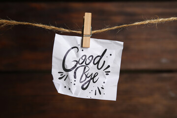 Crumpled paper note with word Goodbye hanging on twine against wooden background