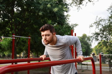 Fototapeta premium Young man doing pull-up on sport ground